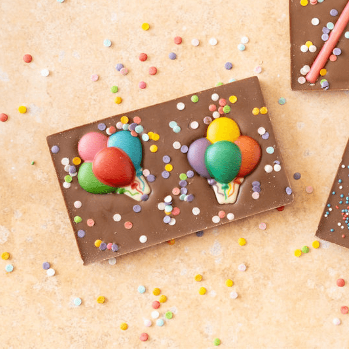 Chocoladereep van melkchocolade met daarop kleurrijke chocoladebalonnen en suikerconfetti.